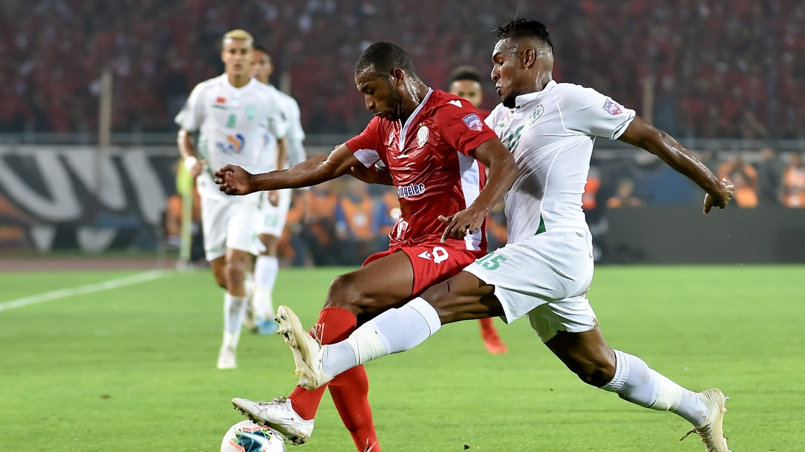 Intense soccer match between Moroccan and Tunisian players on a stadium field during a night game.