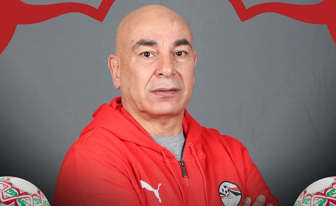 Entraîneur de football marocain avec le logo de l'équipe nationale et deux ballons de la Coupe d'Afrique des Nations en arrière-plan.