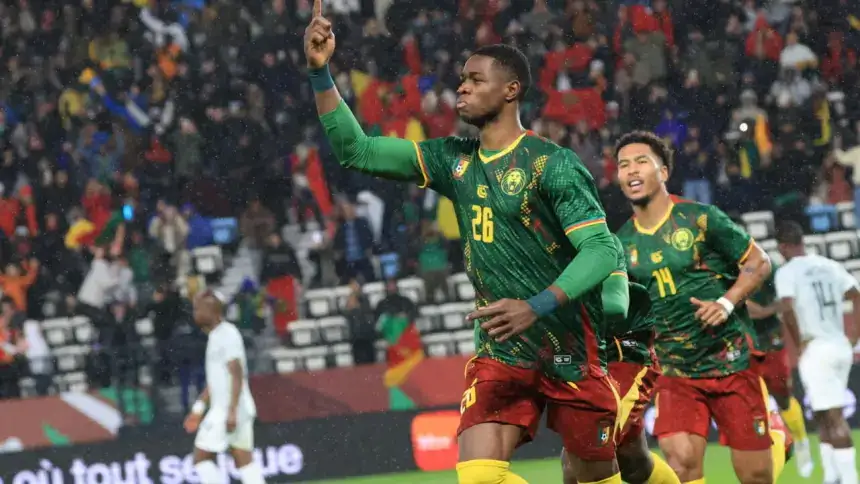 Cameroonian forward celebrates a goal in a vibrant green kit, with jubilant teammates in a lively stadium backdrop during a rain-soaked match.
