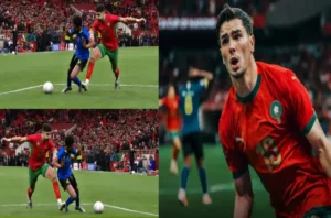 Morocco's player in red battles for the ball against a blue-clad opponent, showcasing intense match action amid a vibrant stadium crowd.