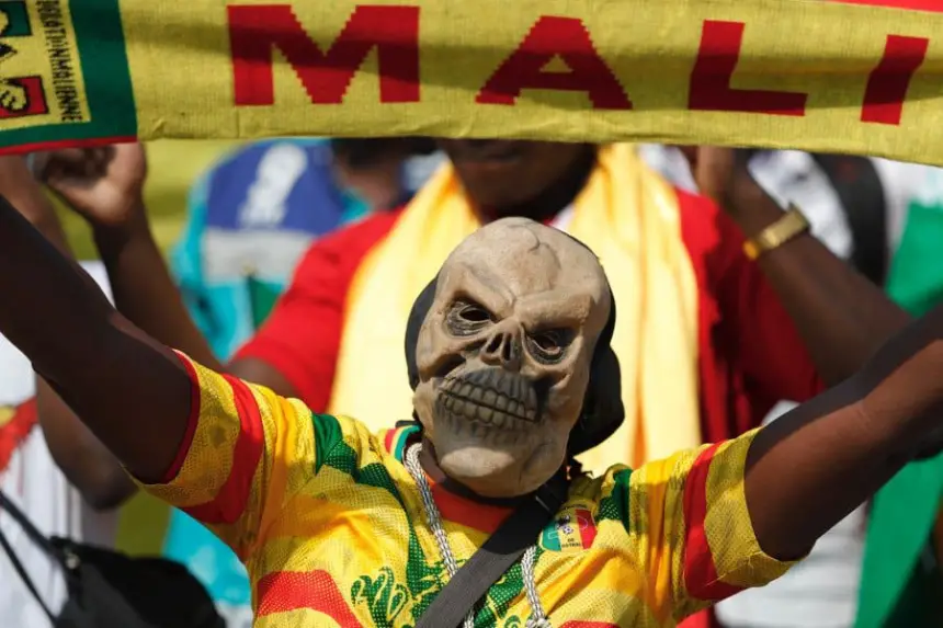 Un fan malien en maillot vibrant agite une écharpe jaune "MALI", portant un masque de crâne distinctif, montrant l'esprit d'équipe pendant un match.