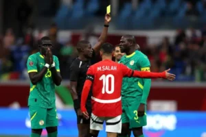 Referee issues a yellow card as Mohamed Salah (Egypt, number 10) protests near Senegalese players during a tense match moment.
