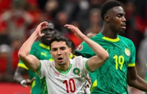 Le joueur marocain numéro 10 réagit durant un moment de tension, encadré par le numéro 19 sénégalais, dans le cadre dynamique d'un match de la CAN.