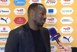 Moroccan footballer being interviewed on a vibrant orange backdrop featuring sponsor logos, showcasing key moments from a post-match discussion.