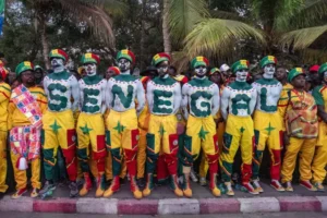 Des supporters sénégalais, vêtus d'atours festifs jaunes et verts, le corps peint formant le mot 'SENEGAL', unis dans la célébration avant un match de football.