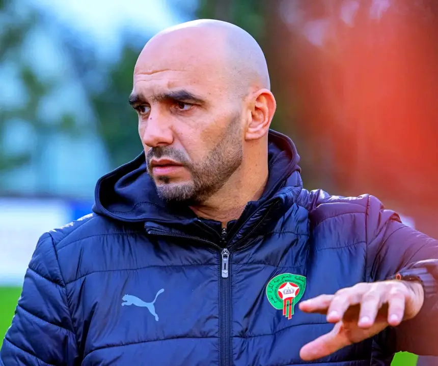 Walid Regragui, sélectionneur de l'équipe nationale du Maroc, gesticule lors d'une séance d'entraînement, portant une veste noire Puma arborant l'emblème marocain.