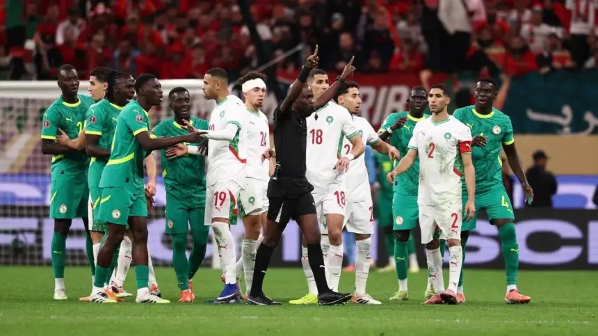 Morocco and Senegal players argue with the referee during a tense moment in their international match, showcasing vibrant team kits and stadium atmosphere.