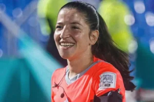 Smiling female referee in a bright orange kit, officiating a football match, showcasing the spirit of inclusivity in Moroccan sports.