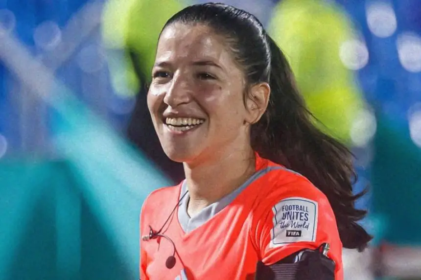 Smiling female referee in a bright orange kit, officiating a football match, showcasing the spirit of inclusivity in Moroccan sports.