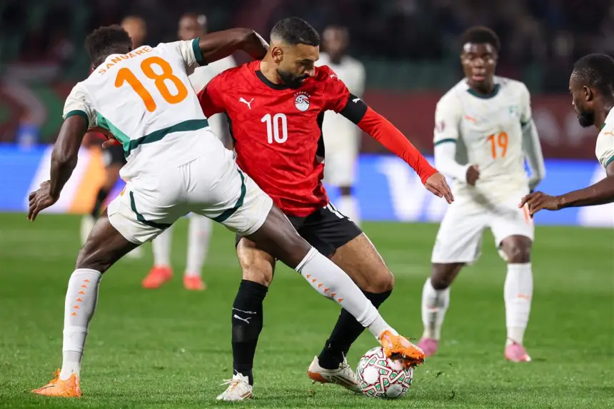Mohamed Salah d'Égypte, en tenue rouge, se bat pour le ballon contre Samuel de la Côte d'Ivoire, qui porte une tenue blanche avec des détails orange, lors d'un match tendu.