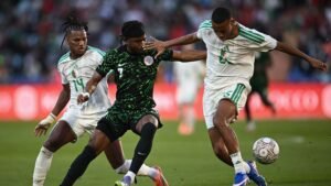 Un joueur nigérian en maillot vert lutte contre des adversaires algériens en blanc pendant un moment tendu du match, avec le ballon en jeu.