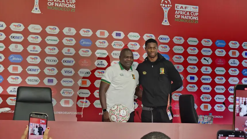 مدرب ولاعب كاميرونيان يلتقيان للتصوير معاً في مؤتمر صحفي لكأس الأمم الأفريقية 2025 بالمغرب، مع ظهور شعارات الرعاة.