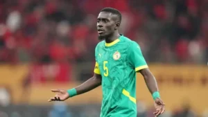 Senegalese player wearing a green jersey with yellow accents, gesturing during a match, amid a vibrant stadium atmosphere.