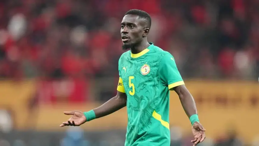 Senegalese player wearing a green jersey with yellow accents, gesturing during a match, amid a vibrant stadium atmosphere.