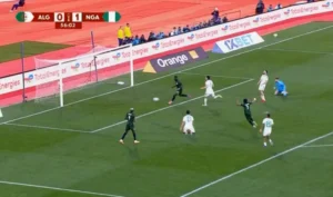 Nigerian players in green defend against an Algerian attack, with the score at 0-1 during a tense international match.