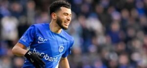 Ziyad Laaroubi celebrates after scoring for KRC Genk, wearing a blue kit with the club logo, in a lively stadium atmosphere.