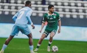 Mahdi Benoun dribbling the ball in a green kit, opposing a player in sky blue, during a thrilling football match.