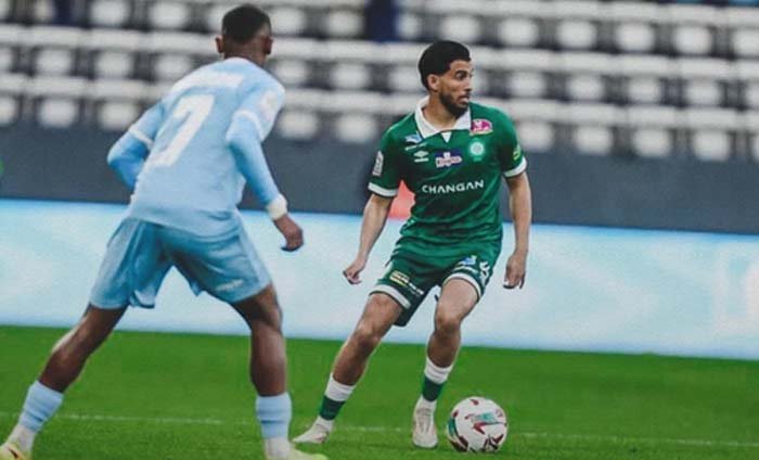 Mahdi Benoun dribbling the ball in a green kit, opposing a player in sky blue, during a thrilling football match.