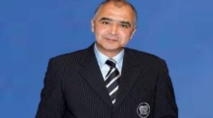 FIFA official in a pinstripe suit, smiling against a solid blue background, representing Moroccan football governance.