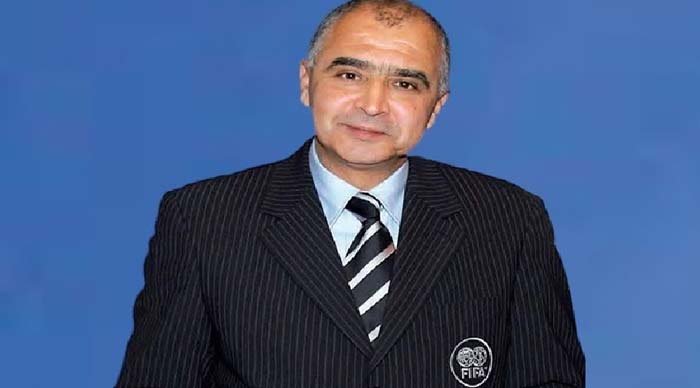 FIFA official in a pinstripe suit, smiling against a solid blue background, representing Moroccan football governance.