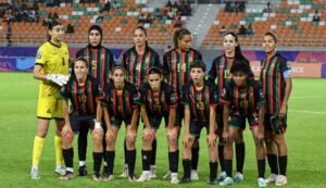 Morocco's women's football team in their distinctive red, green, and black kit, posing together on the pitch, ready for competition.