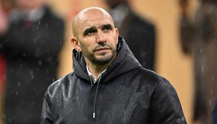 Walid Regragui, head coach of the Moroccan national football team, looks pensive in the rain, wearing a dark hoodie.