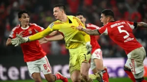 Benfica goalkeeper in a yellow kit gesturing during UEFA Champions League match, surrounded by teammates in red kits and opponents in white.