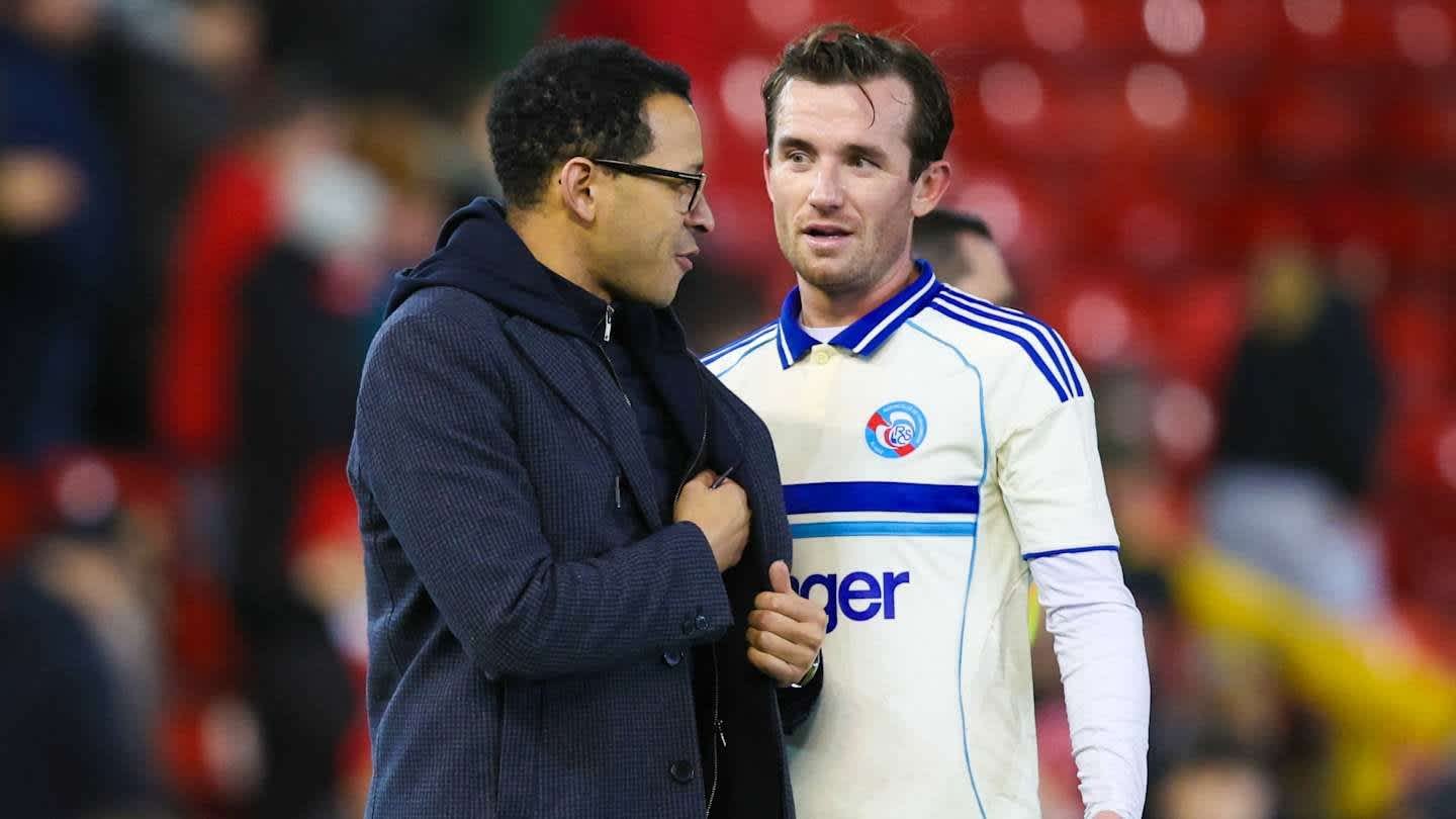 Liam Rosenior de Strasbourg converse avec un officiel du club, tous deux souriants, sur fond d'un stade en train d'applaudir.