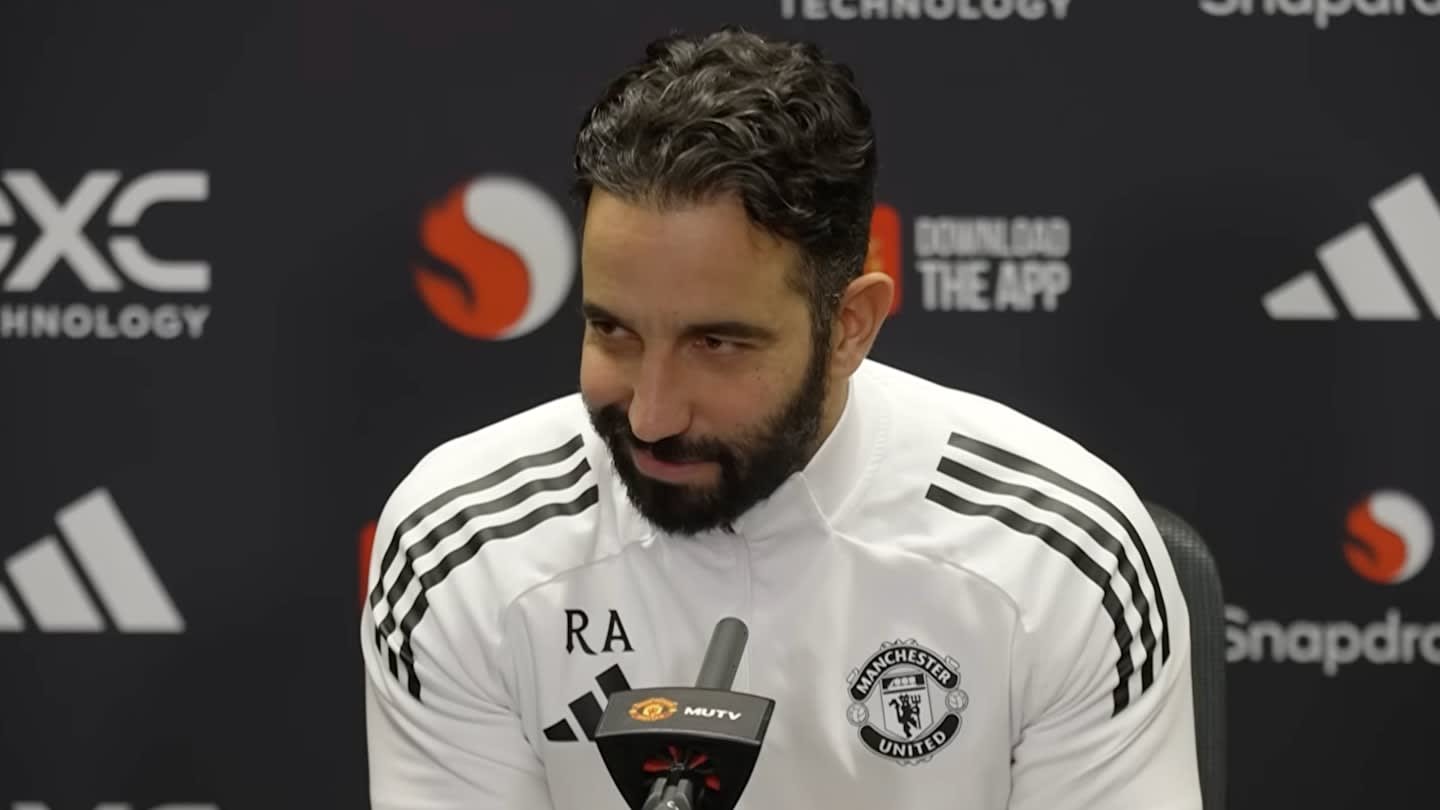 Rúben Amorim, portant un maillot d'entraînement de Manchester United, sourit lors d'une conférence de presse avec l'identité du club et les sponsors en arrière-plan.