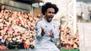 زيركزي يحتفل بشغف بزي كرة القدم الأبيض، مشيراً نحو الجمهور في أجواء ملعب نابضة بالحياة.