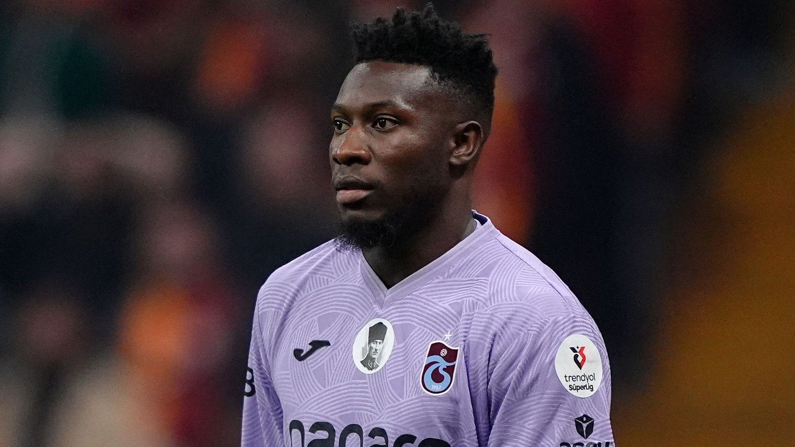 Andre Onana in een paars Trabzonspor-tenue; een geconcentreerde uitdrukking tijdens een wedstrijd, die zijn rol als prominent doelman benadrukt.