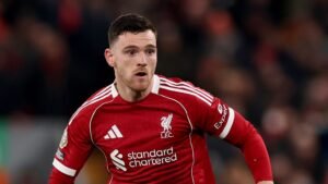 Liverpool's Andrew Robertson in een rood tenue tijdens een wedstrijd, vastberadenheid tonend terwijl hij speelt, met een vervaagde stadionachtergrond.