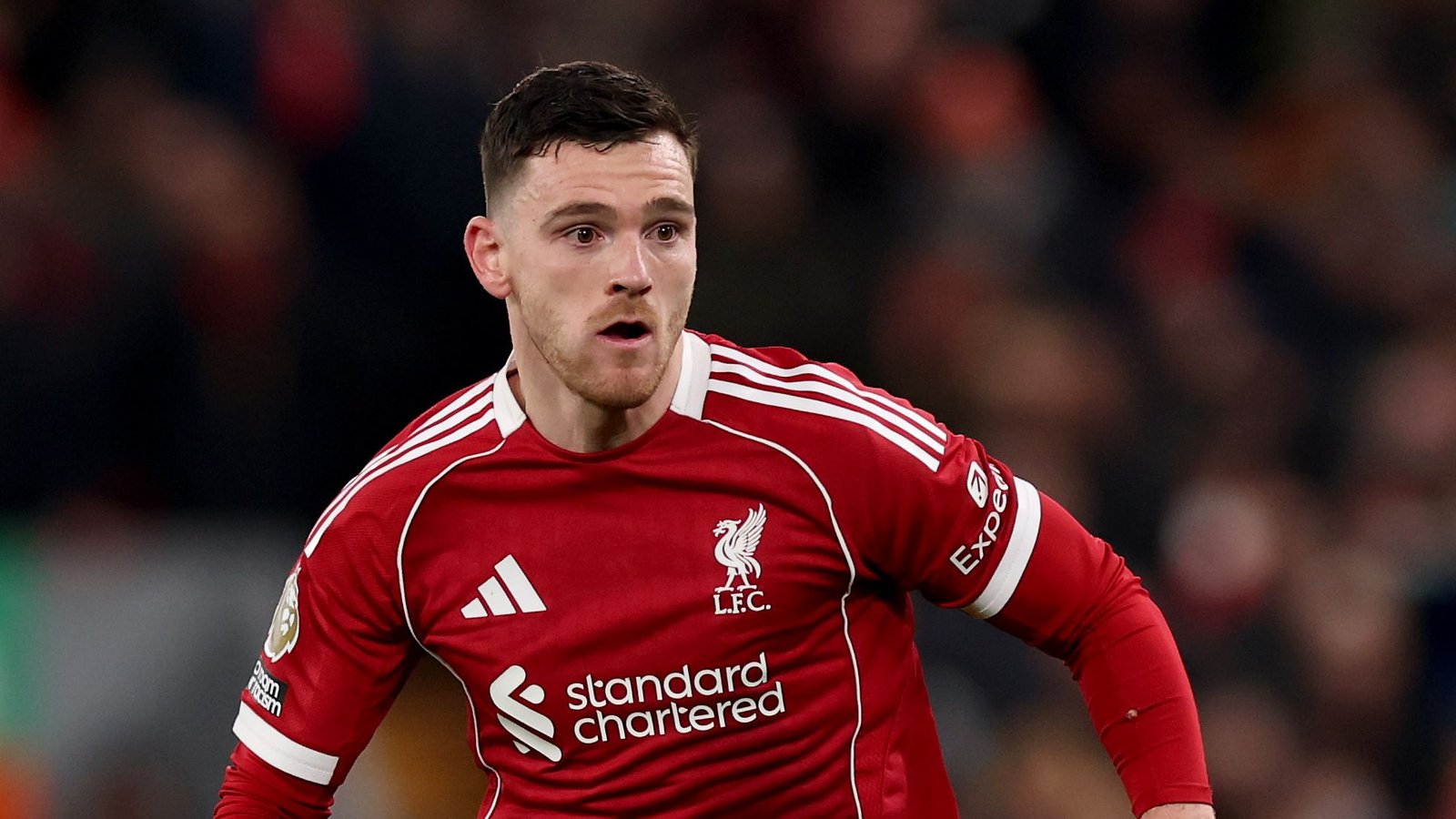 Liverpool's Andrew Robertson in een rood tenue tijdens een wedstrijd, vastberadenheid tonend terwijl hij speelt, met een vervaagde stadionachtergrond.