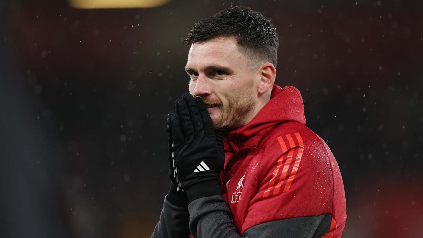 Andy Robertson, wearing a red Liverpool training jacket, reacts with his hands to his face, rain visible in the background.