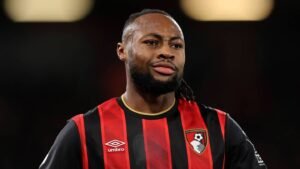 Antoine Semenyo, dans le kit rayé noir et rouge de l'AFC Bournemouth, se concentre avec une expression sérieuse lors d'un match.