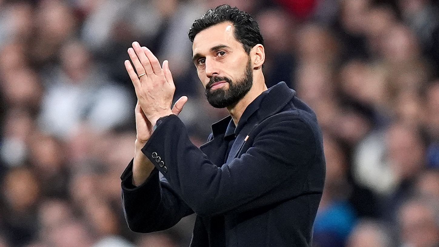 Álvaro Arbeloa die het publiek toejuicht, gekleed in een donkere jas, met een wazig stadion op de achtergrond, een moment van waardering vastleggend.