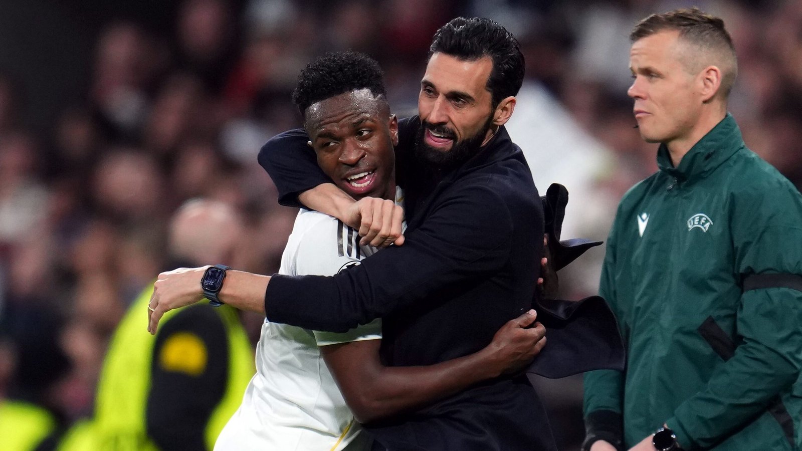 Vinícius Júnior viert uitbundig met een teamgenoot, terwijl een UEFA-functionaire toekijkt, wat de kameraadschap tijdens een wedstrijd van Real Madrid benadrukt.