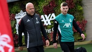 Arne Slot et Andy Robertson s'entretiennent sur l'entraînement de Liverpool, entourés de verdure et de l'identité du club au Centre d'Entraînement AXA.