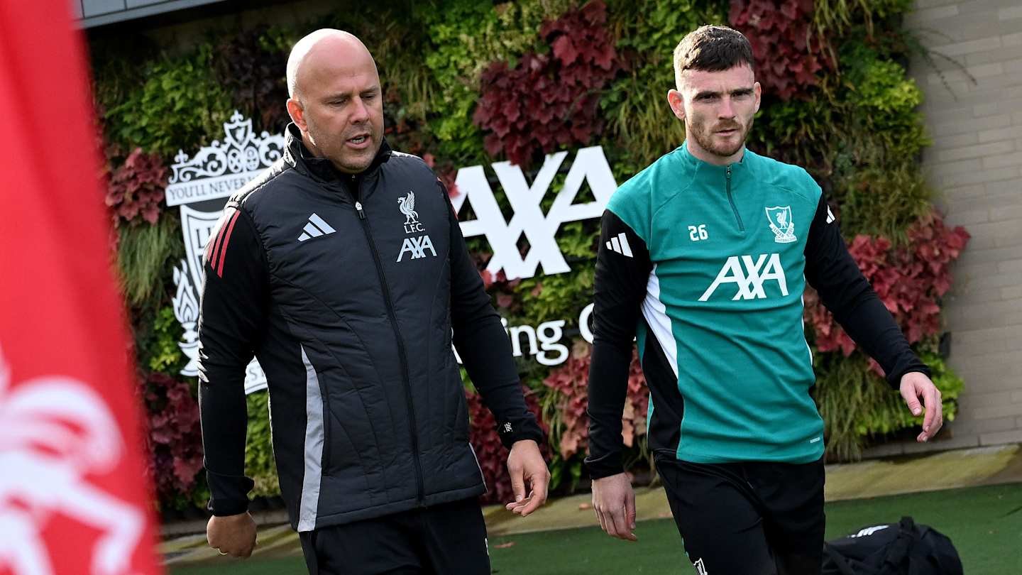 Arne Slot et Andy Robertson s'entretiennent sur l'entraînement de Liverpool, entourés de verdure et de l'identité du club au Centre d'Entraînement AXA.