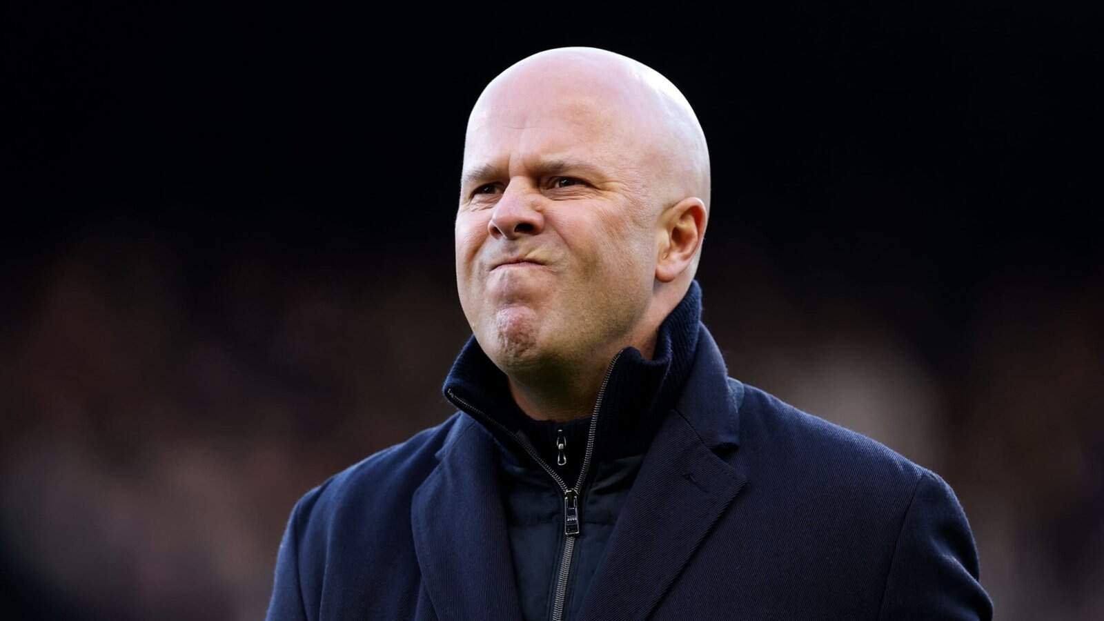 Homme chauve portant un manteau sombre, probablement un entraîneur sportif, avec une expression concentrée.