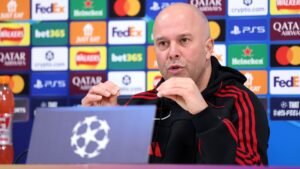 Arne Slot speaks during a press conference, with a UEFA Champions League backdrop featuring various sponsorship logos.