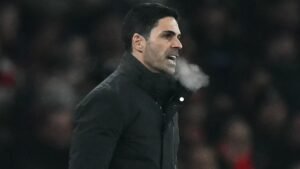 Mikel Arteta, in een donkere jas, instrueert zijn team gepassioneerd vanaf de zijlijn, waarbij zijn adem zichtbaar is in de koude atmosfeer.