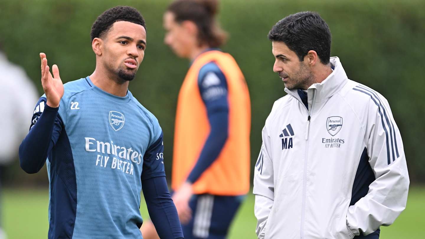 Ethan Nwaneri and Mikel Arteta converse during an Arsenal training session, both in club attire, with a green background.