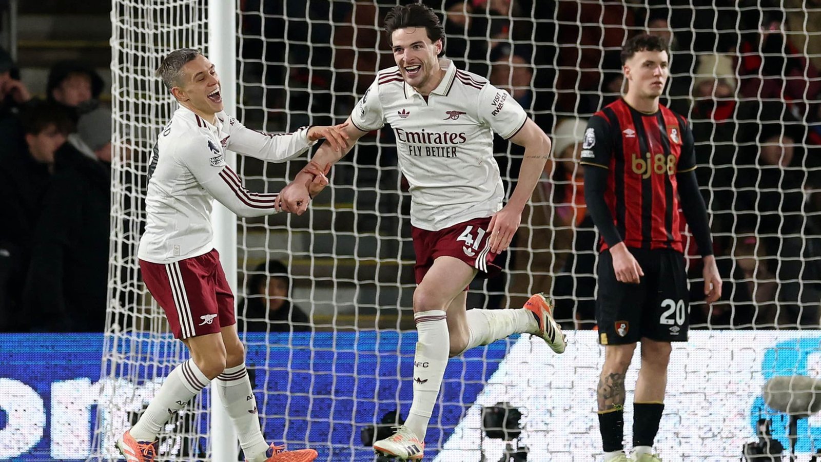 Declan Rice viert een doelpunt met een teamgenoot tijdens Arsenal's wedstrijd tegen Bournemouth, terwijl een Bournemouth-speler toekijkt.