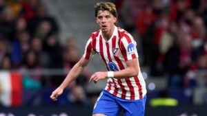 Conor Gallagher in het rood-wit gestreepte tenue van Atlético Madrid, actief spelend tijdens een wedstrijd, met fans op de achtergrond.