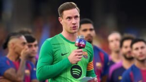 Marc-André ter Stegen en tenue de gardien s'adressant aux supporters avec un micro, ses coéquipiers du Barça en arrière-plan, les couleurs vives de l'équipe visibles.