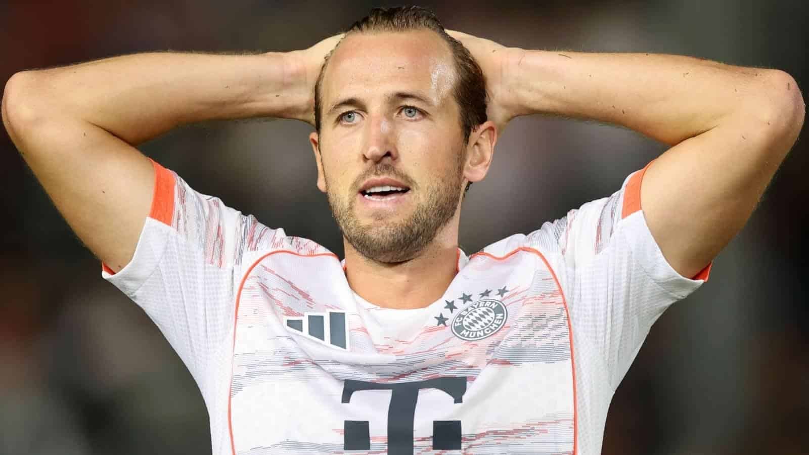 Harry Kane, portant un maillot du Bayern Munich avec des accents orange, semble déçu, se tenant la tête sur le terrain.
