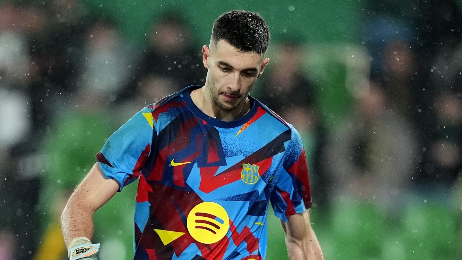 Barcelona-doelman Joan Garcia loopt van het veld in een kleurrijk tenue, terwijl regendruppels om hem heen vallen, wat een gespannen wedstrijdsfeer weerspiegelt.