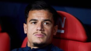 Philippe Coutinho assis sur le banc, l'air contemplatif, portant une tenue d'entraînement marine sur un fond de sièges rouges de stade.
