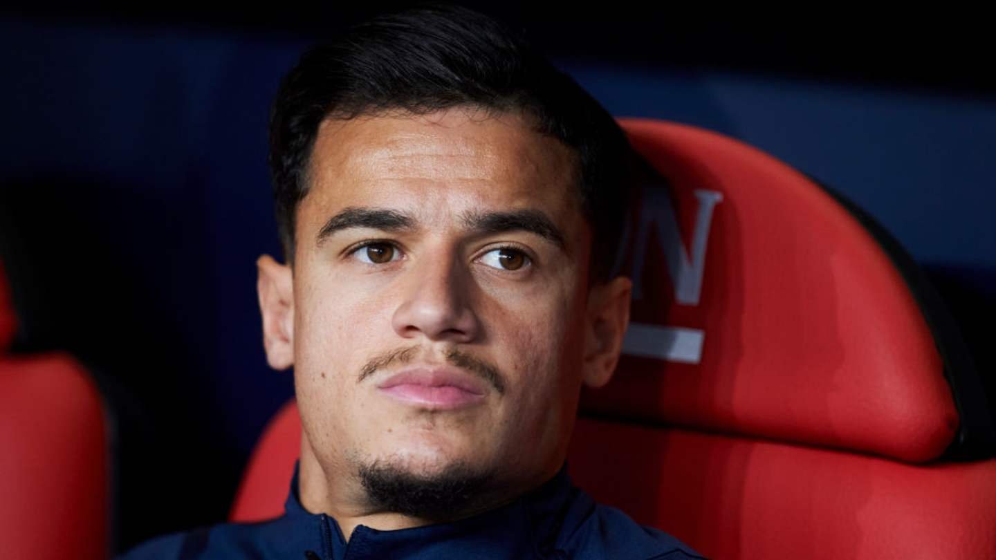 Philippe Coutinho assis sur le banc, l'air contemplatif, portant une tenue d'entraînement marine sur un fond de sièges rouges de stade.